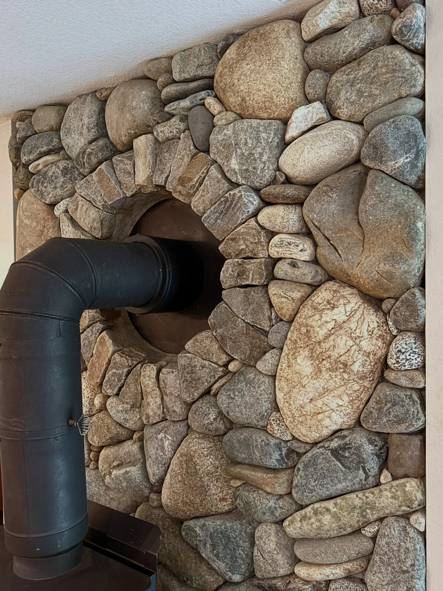 Each new stove pipe presents an artistic opportunity #millerstoneworks #stonemasonry #woodstove #riverrock #interiordesign