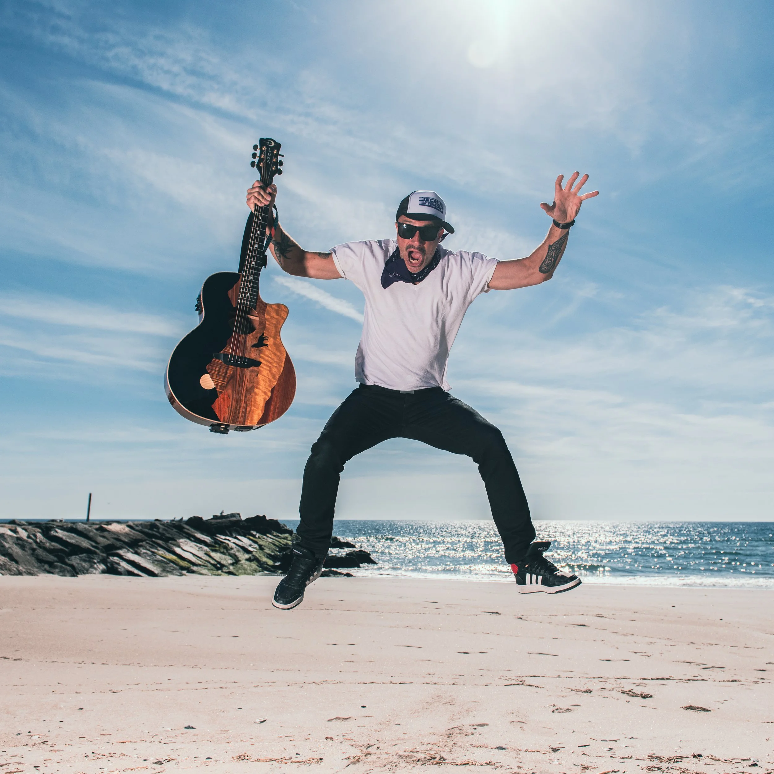 Man with a mustache in a black suit and hat holding an electric guitar, standing against a textured black and white background.