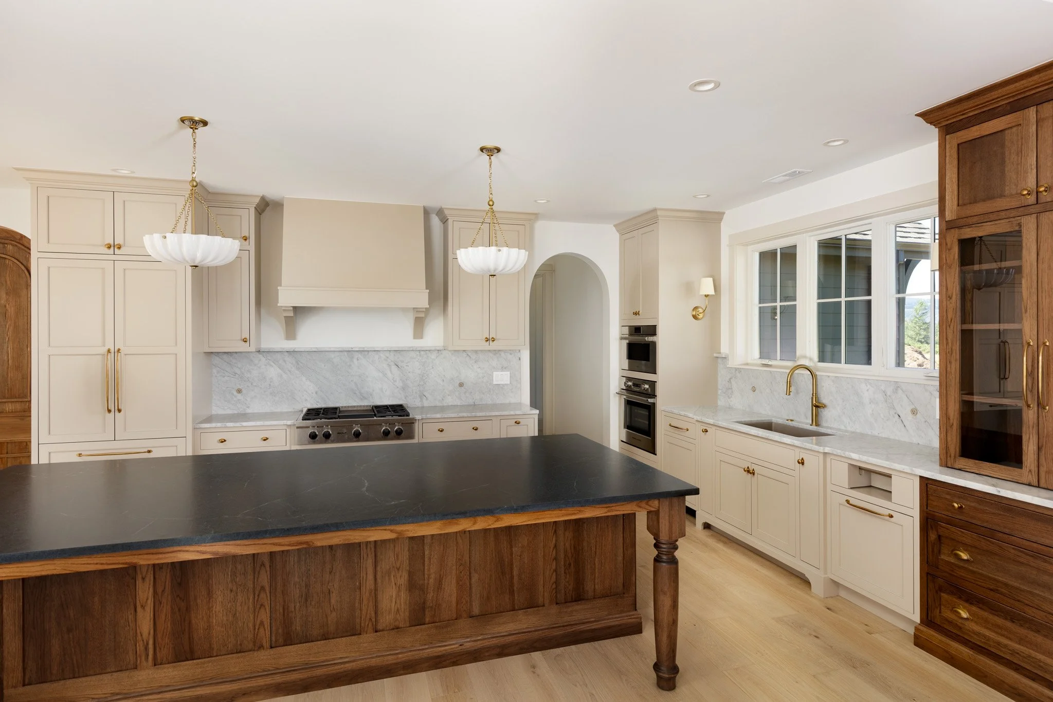 Kitchen with white cabinets, marble backsplash, large window, wooden island, and two pendant lights.