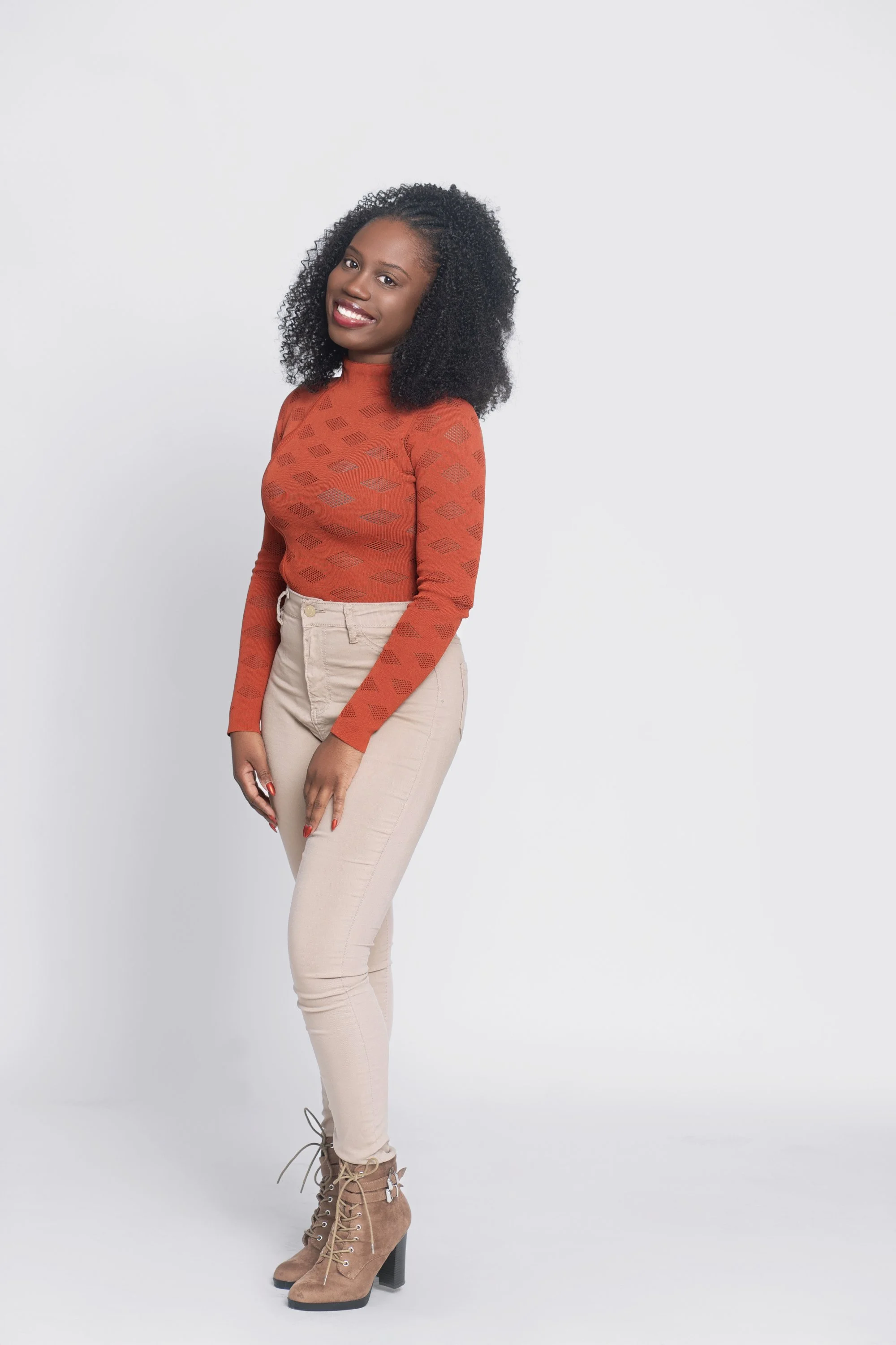 Carmelie with an orange long sleeved shirt, khaki leggings and boots on white background