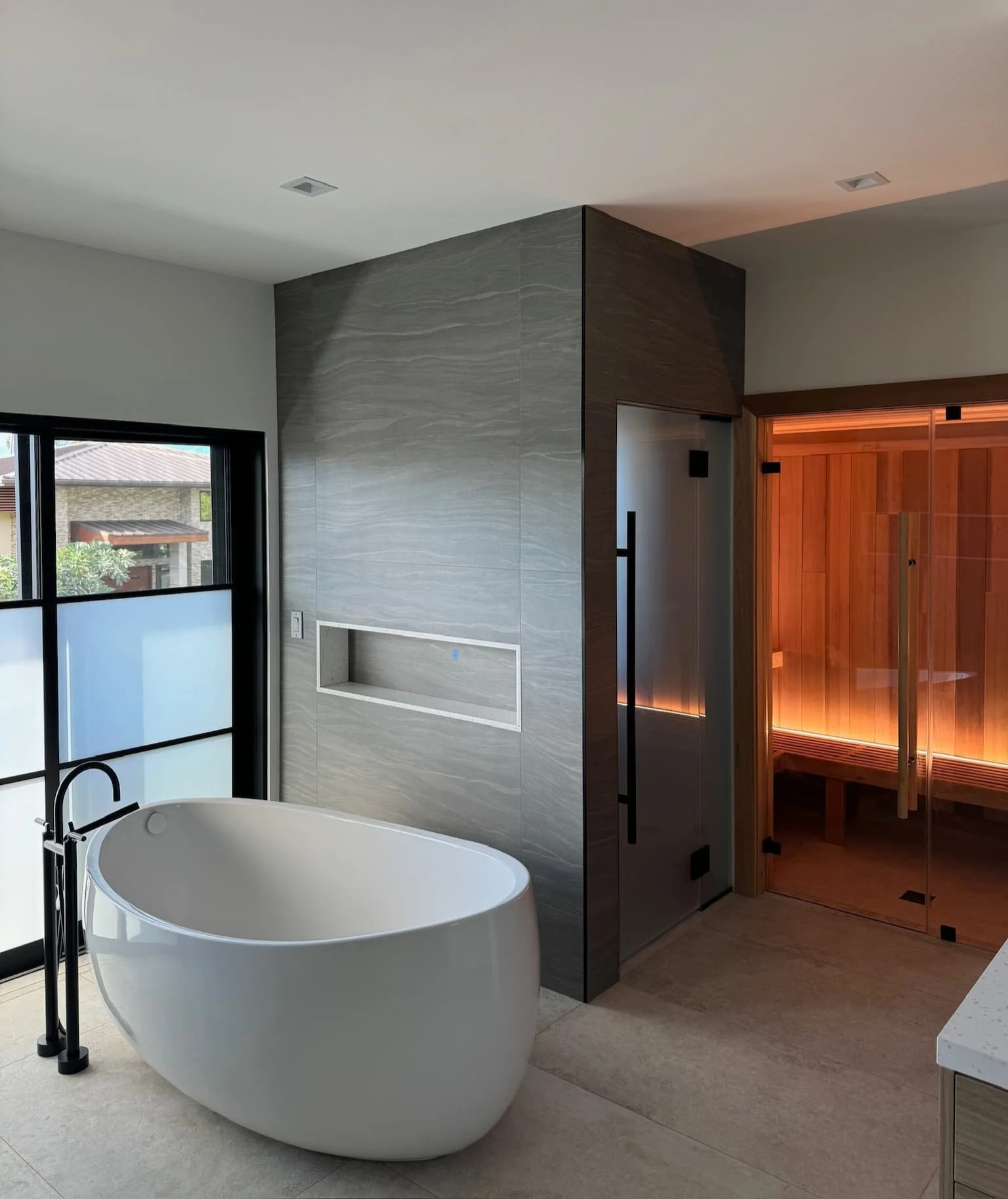 Hale Partners Hawaii Modern bathroom renovation with a freestanding bathtub, a large window, and a wooden sauna with a glass door.