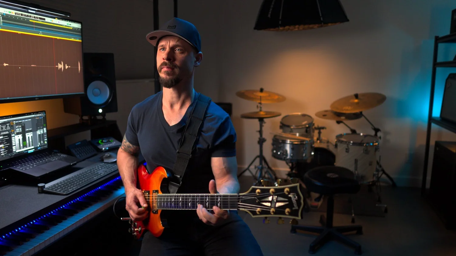 Garrett Ortego holding a guitar in his home studio, with the student dashboard visible on his monitors