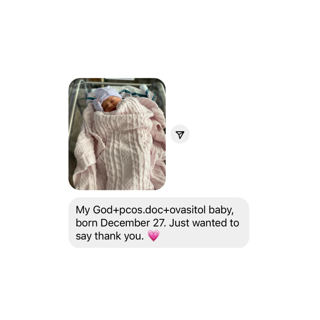 Newborn baby in hospital bassinet, wrapped in a pink sweater, wearing a striped blue and pink hat.