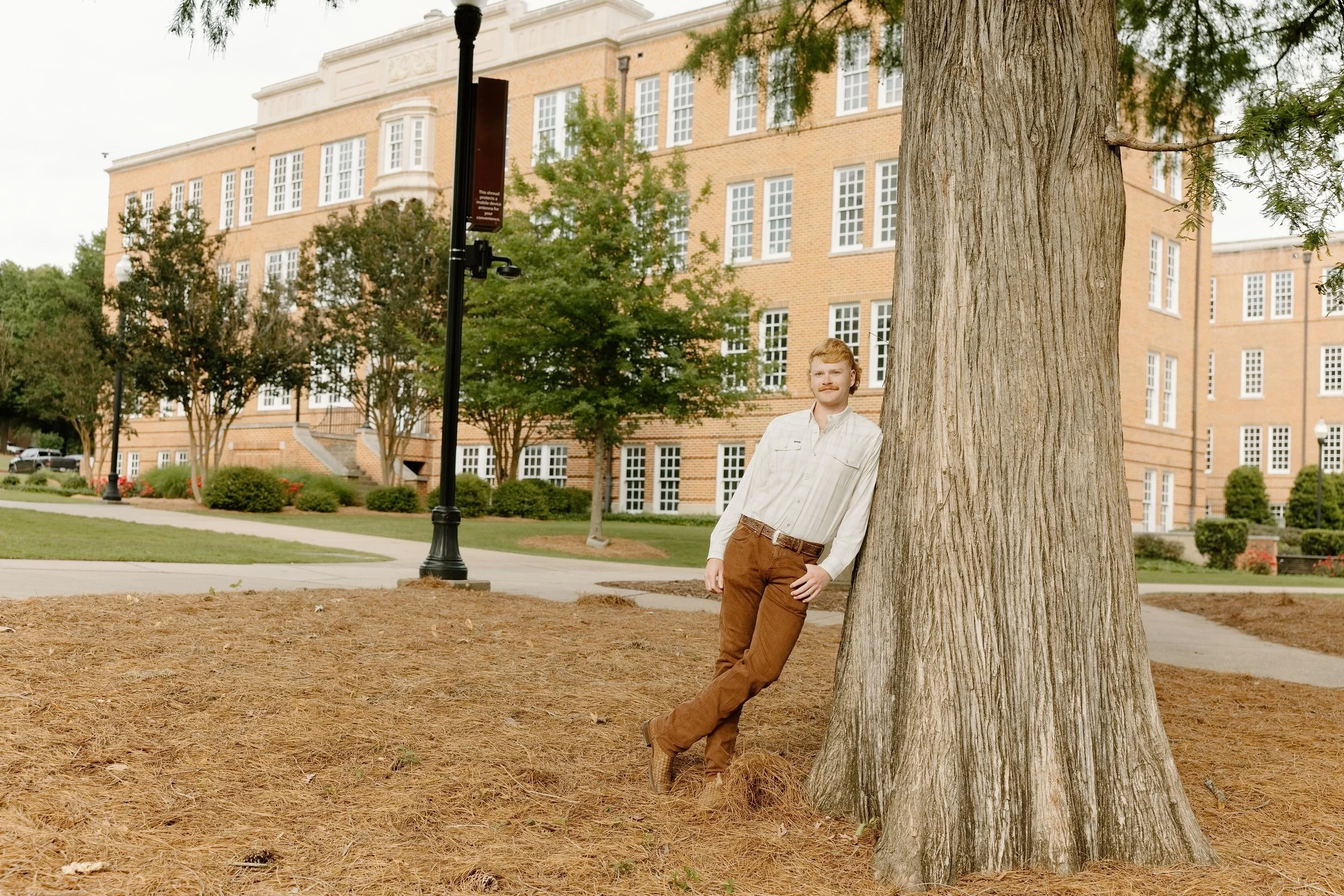 Male grad leaning against tree on Mississippi State campus for graduation