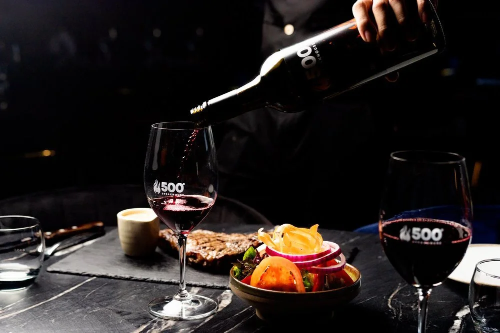 Red wine being poured beside a steak and side dishes at a restaurant