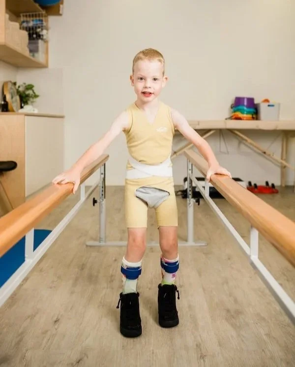 Child in yellow Theratogs garment using parallel bars for gait training and posture support