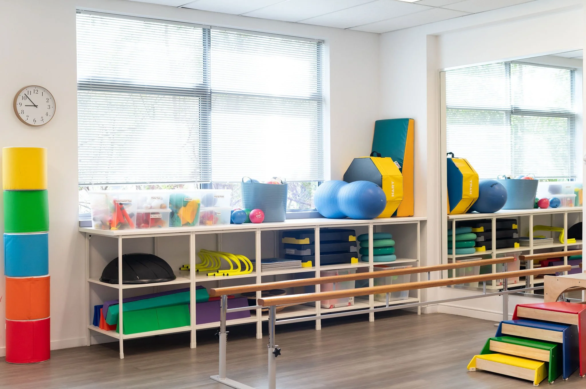 Bright physio clinic room with therapy equipment, toys, and parallel bars