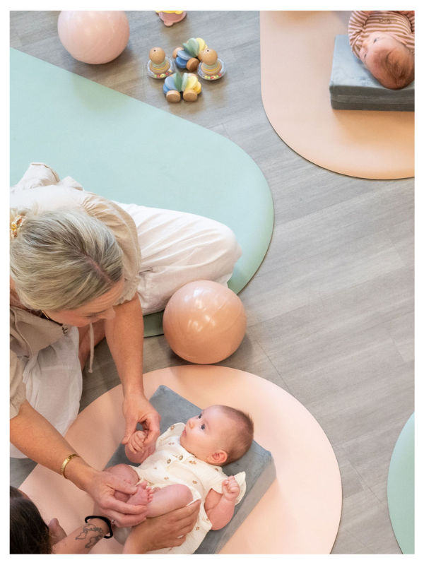 Physiotherapist engaging with a baby during a group session on soft play mats with developmental toys