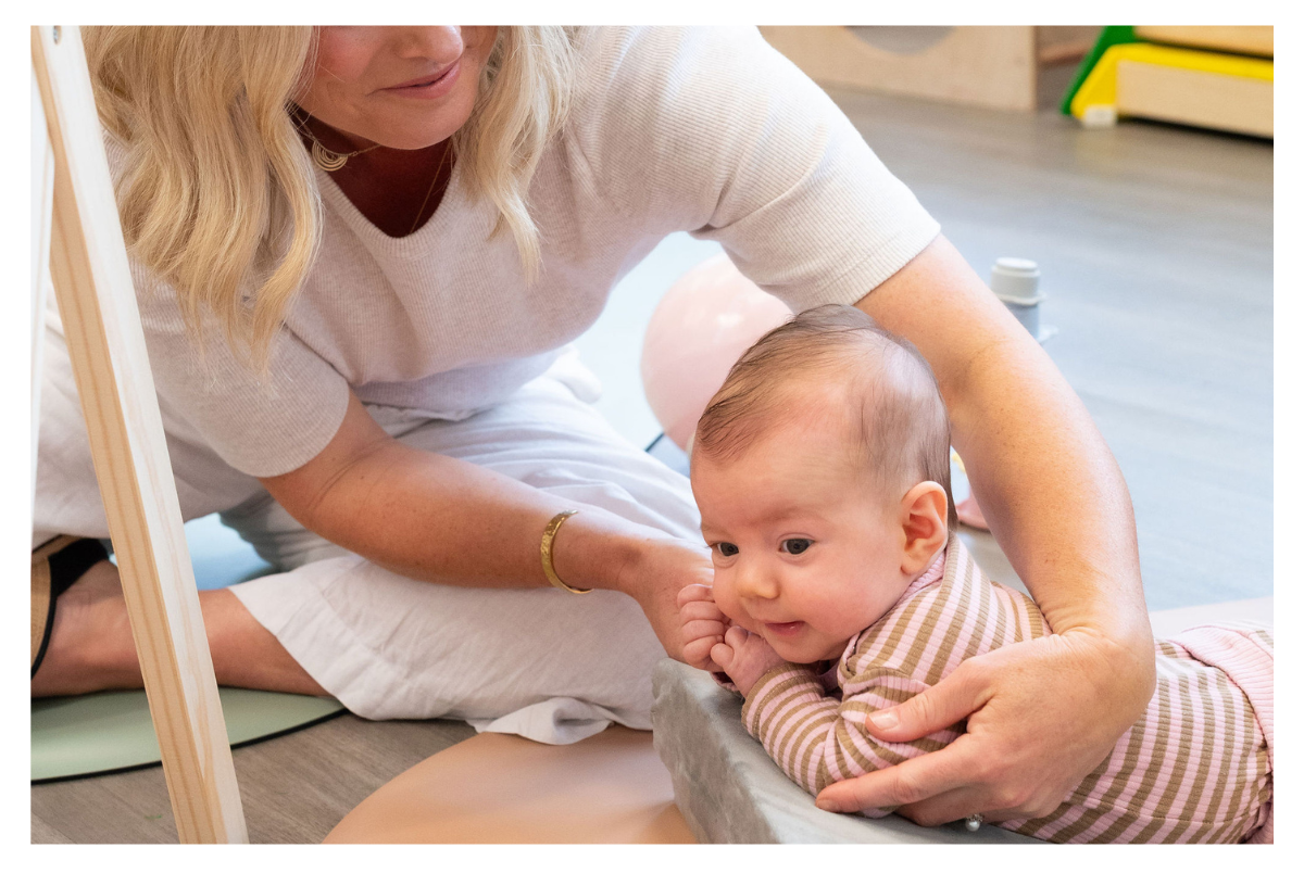 Infant practicing tummy time with gentle support from physiotherapist during developmental session