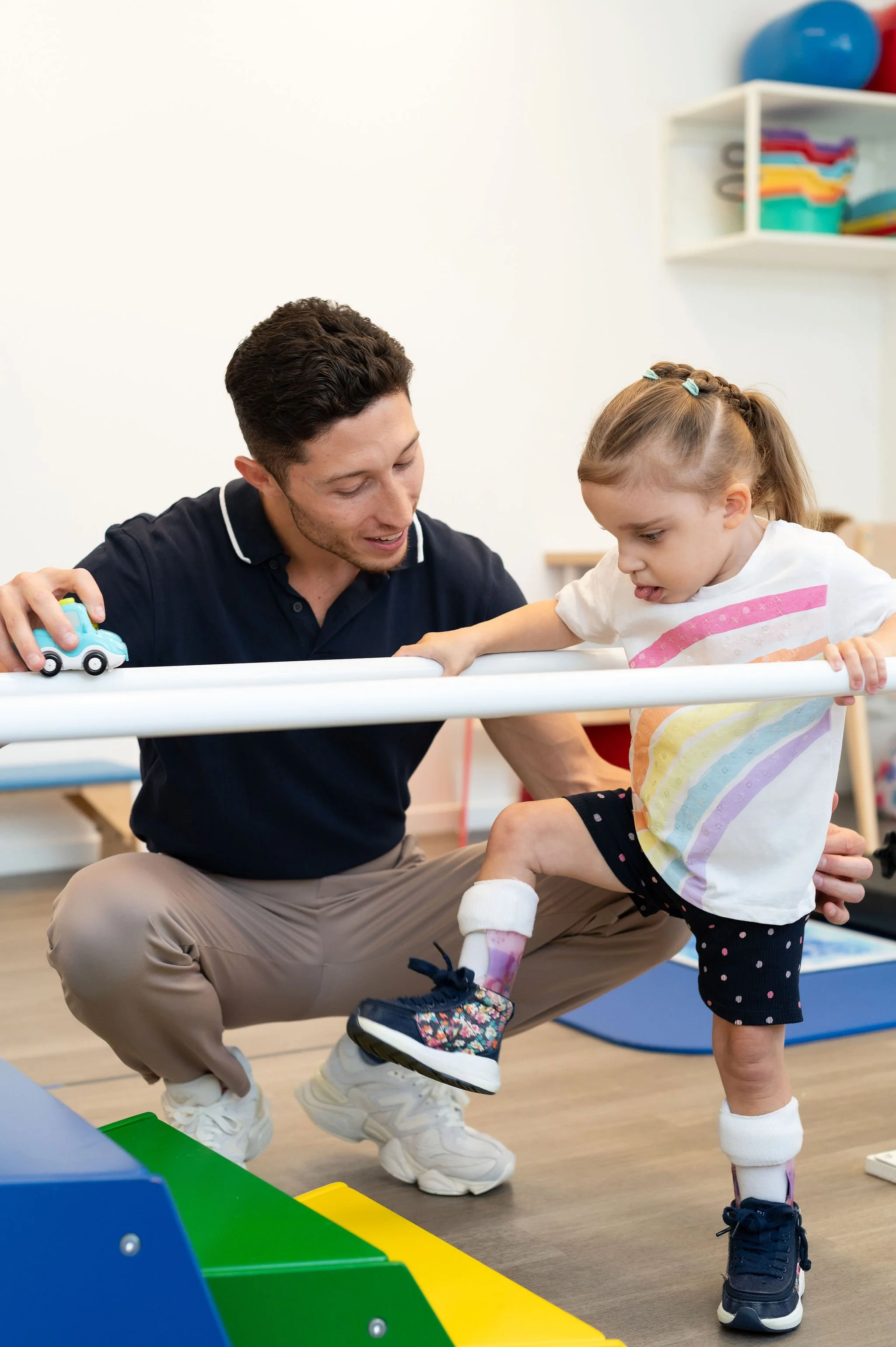 Physiotherapist guiding child to stand using parallel bar during a therapy session