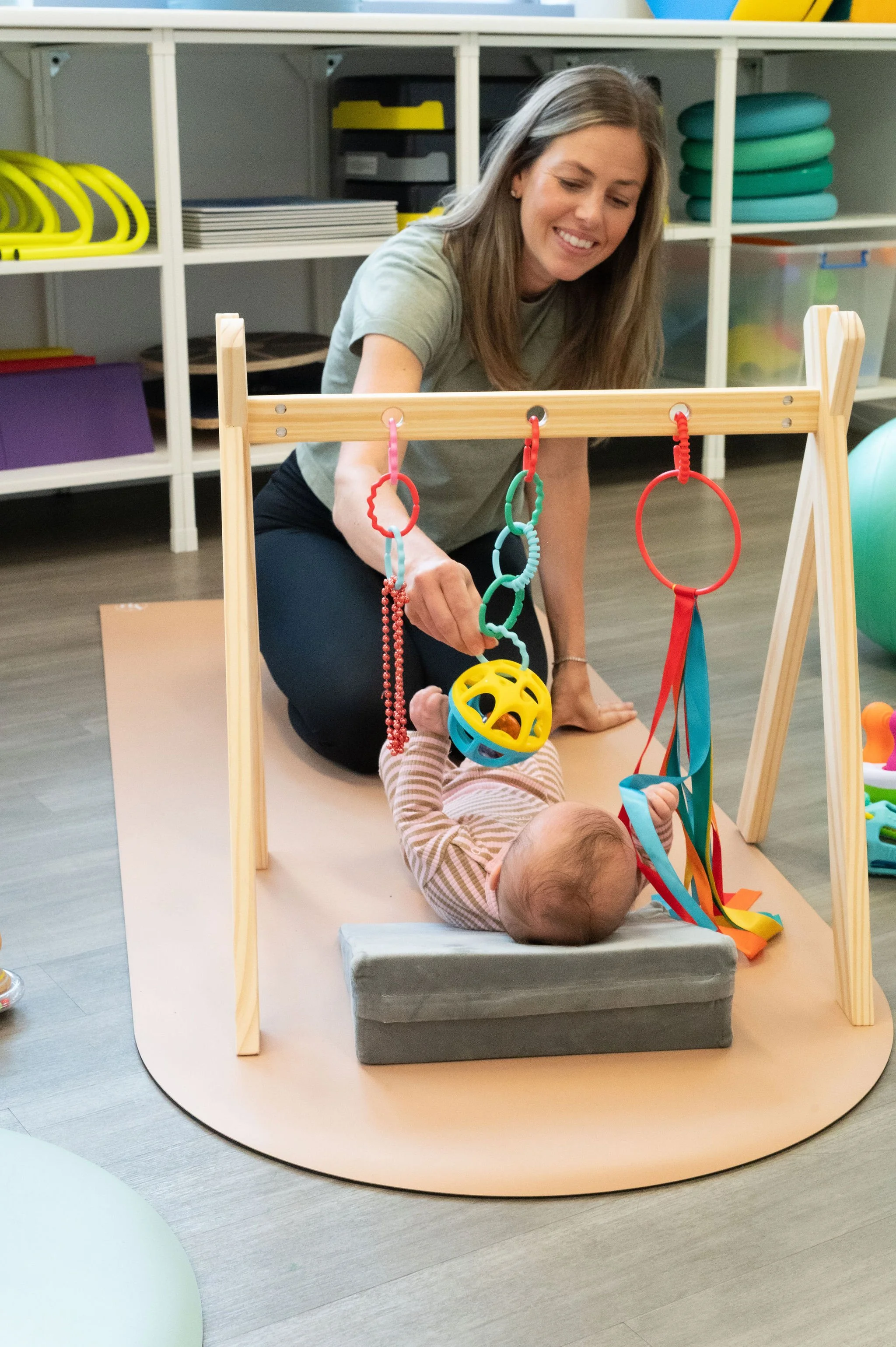 Therapist interacting with baby lying under play gym during movement-focused physio session