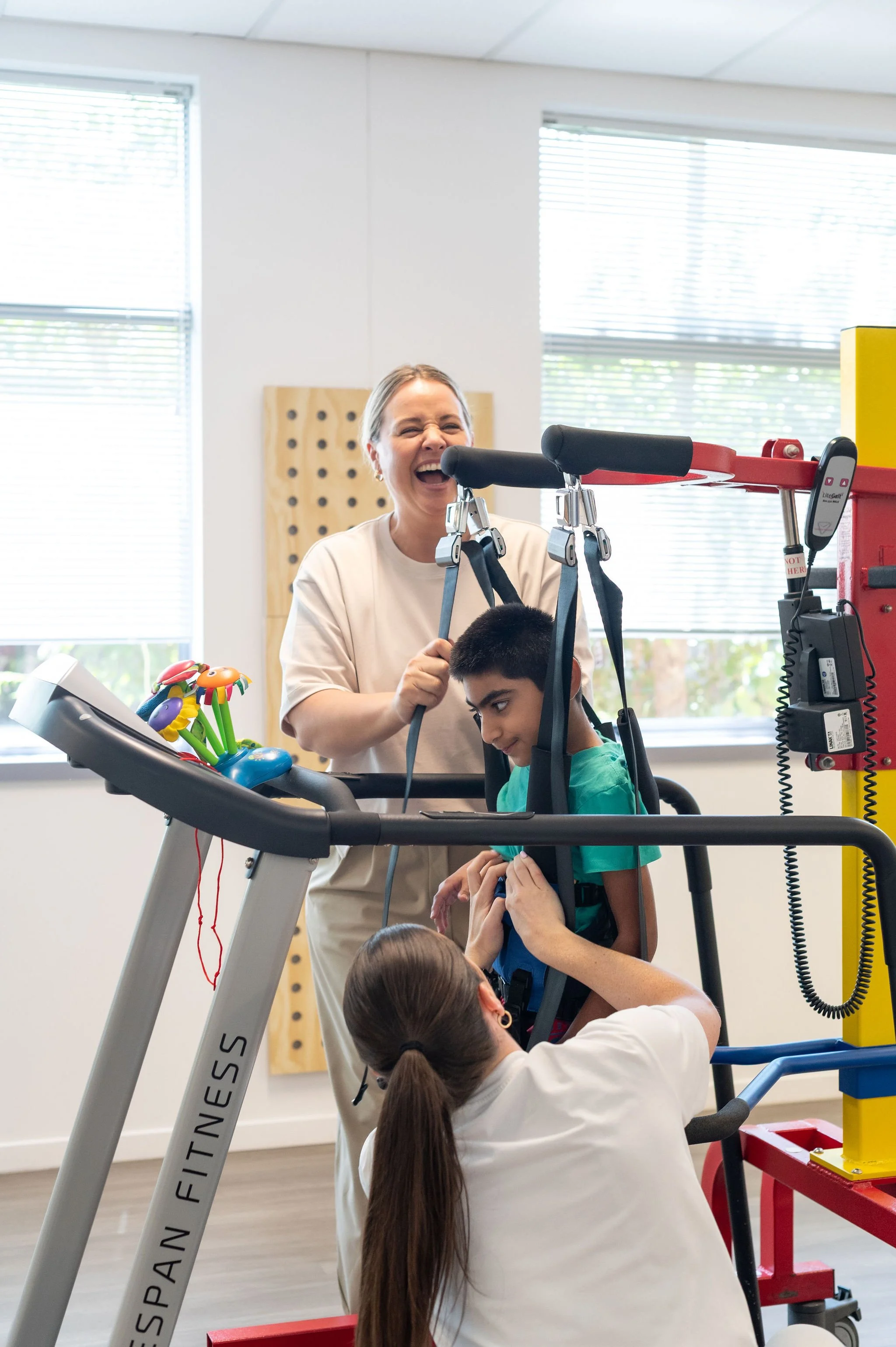 Physiotherapist assisting child with gait training using treadmill and harness support system