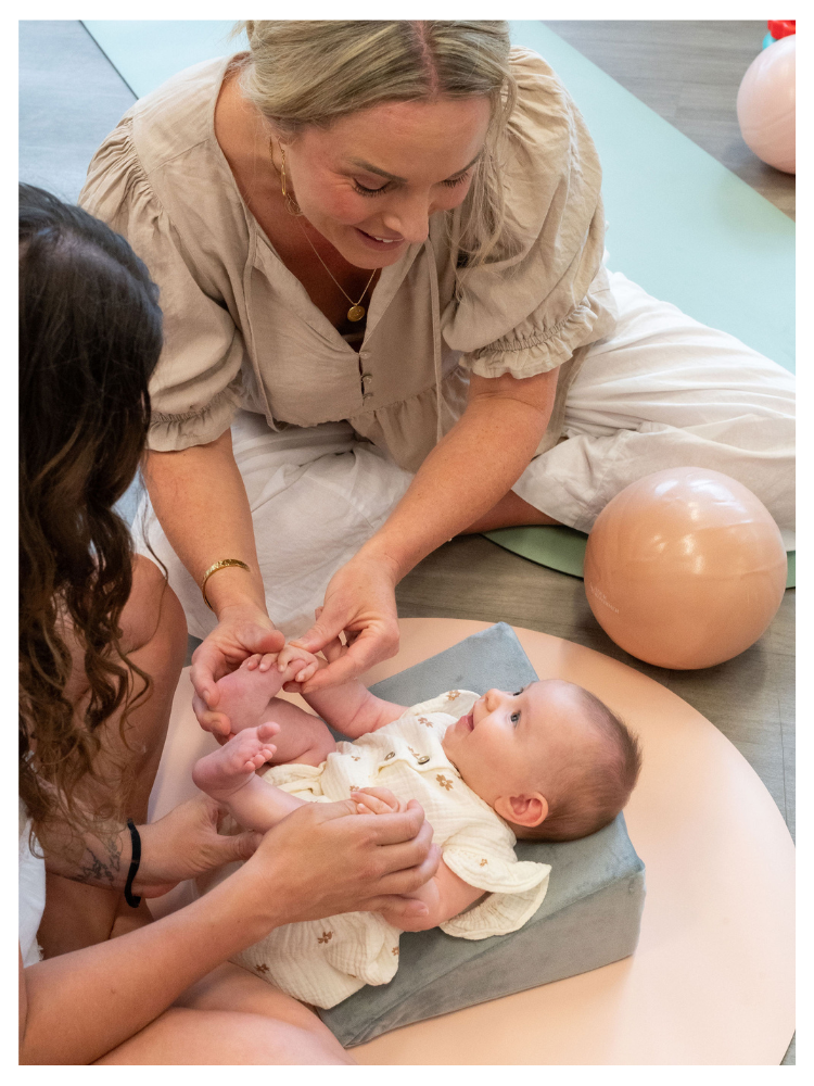 Physiotherapist guiding a baby’s feet and legs during a hands-on therapy session on a soft wedge