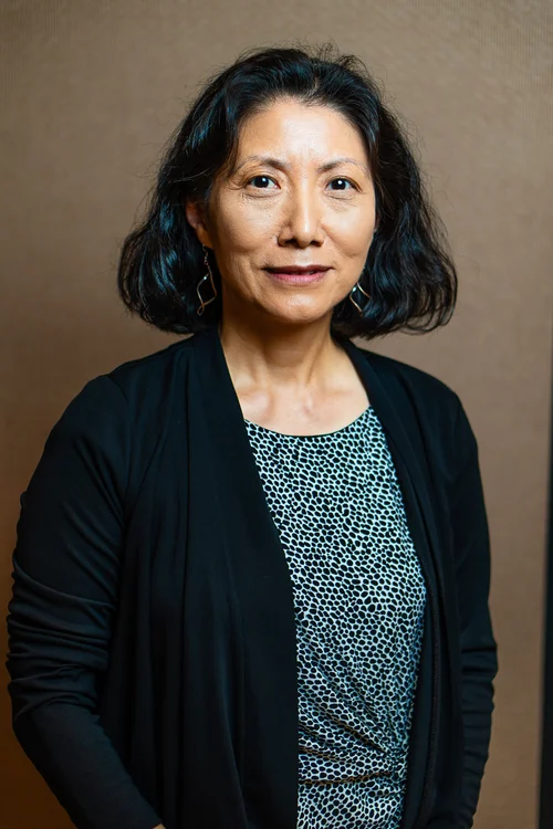 Team headshot of a woman in a black blazer on a brown backdrop