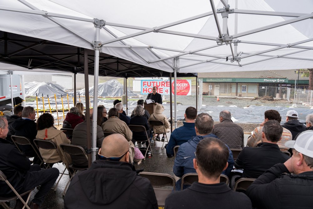Presenter speaking to a seated audience under an event tent