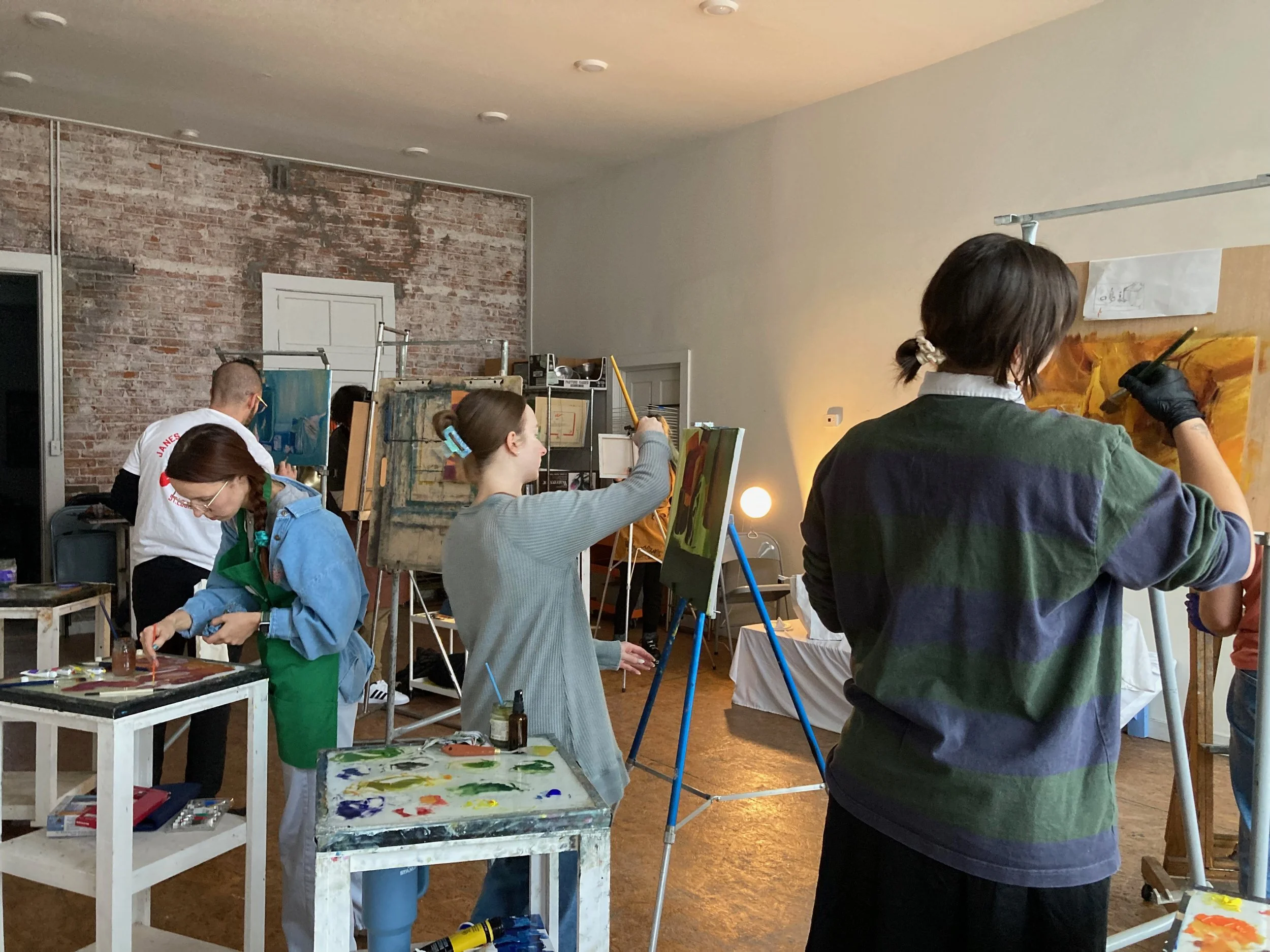 Group of people painting on canvases in an art studio with exposed brick wall