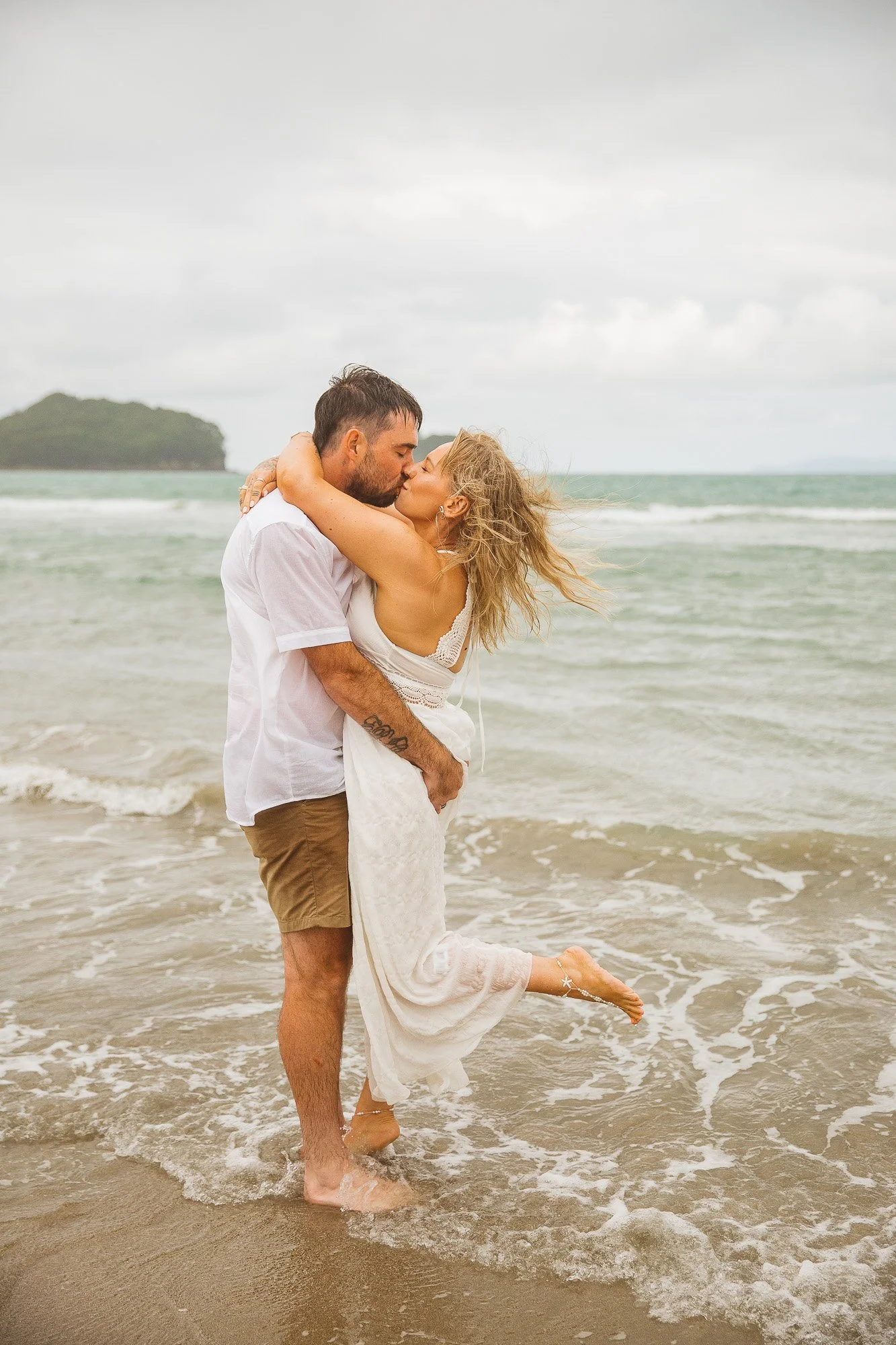 Family gathered on Whangamatā Beach during Ross and Renee’s stormy vow renewal, holding clear umbrellas in the rain.