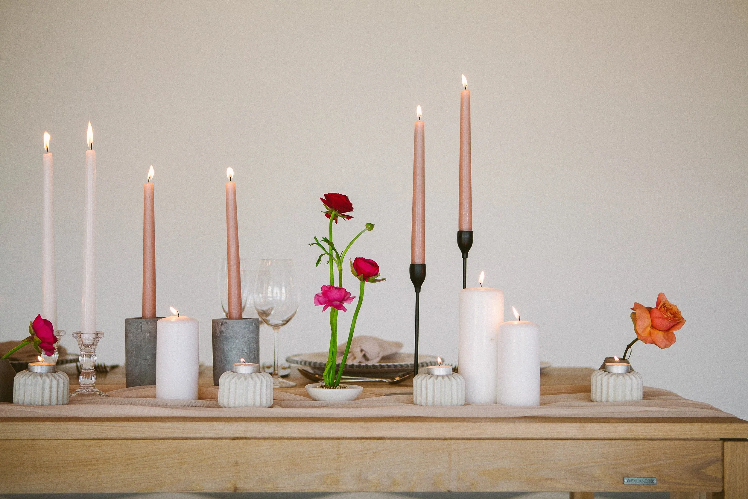 Elegant dining table with lit candles and fresh flowers, including roses, arranged for a cozy setting.
