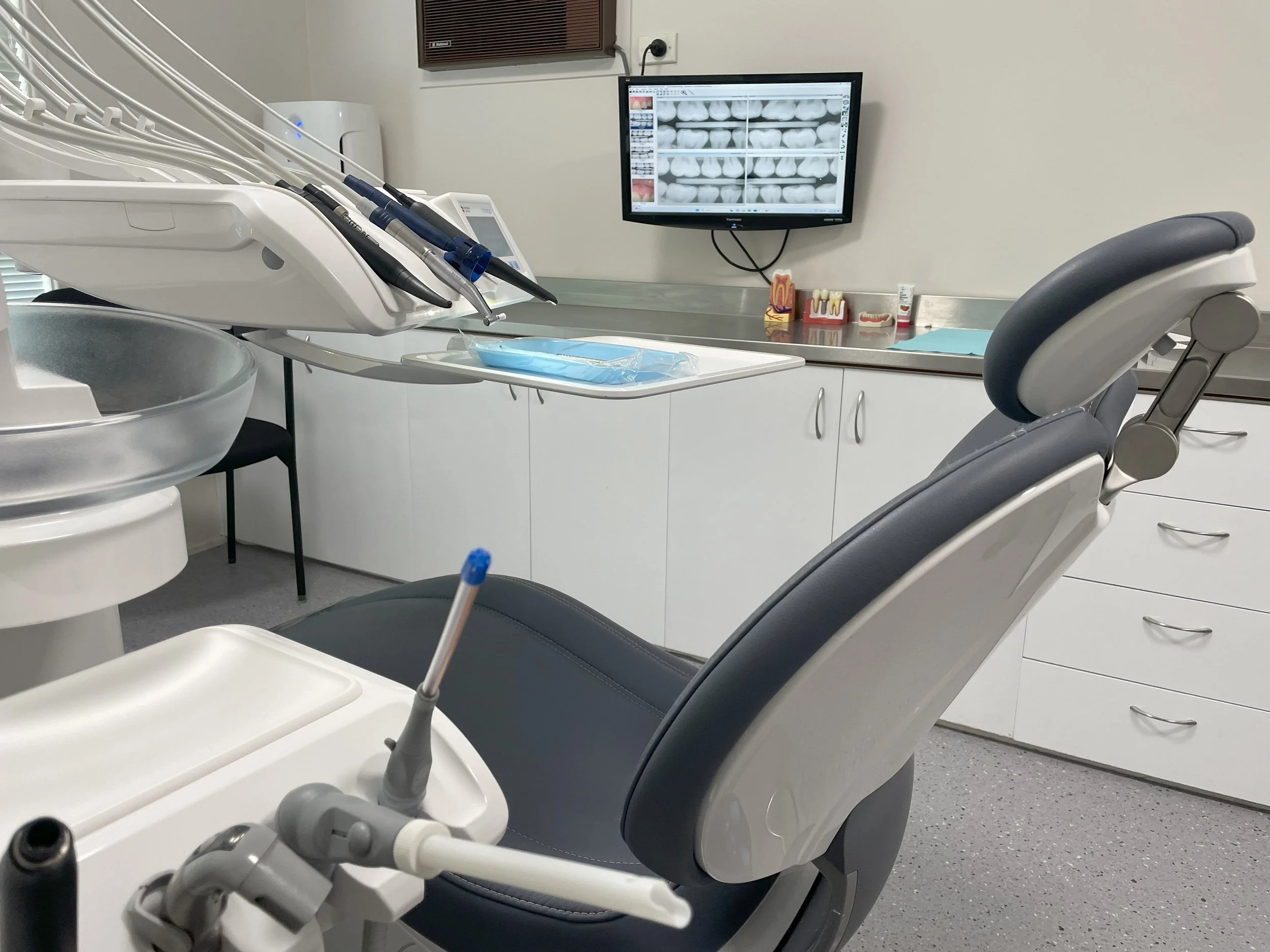 Dental examination room with dental chair, tools, and a monitor displaying dental X-rays.