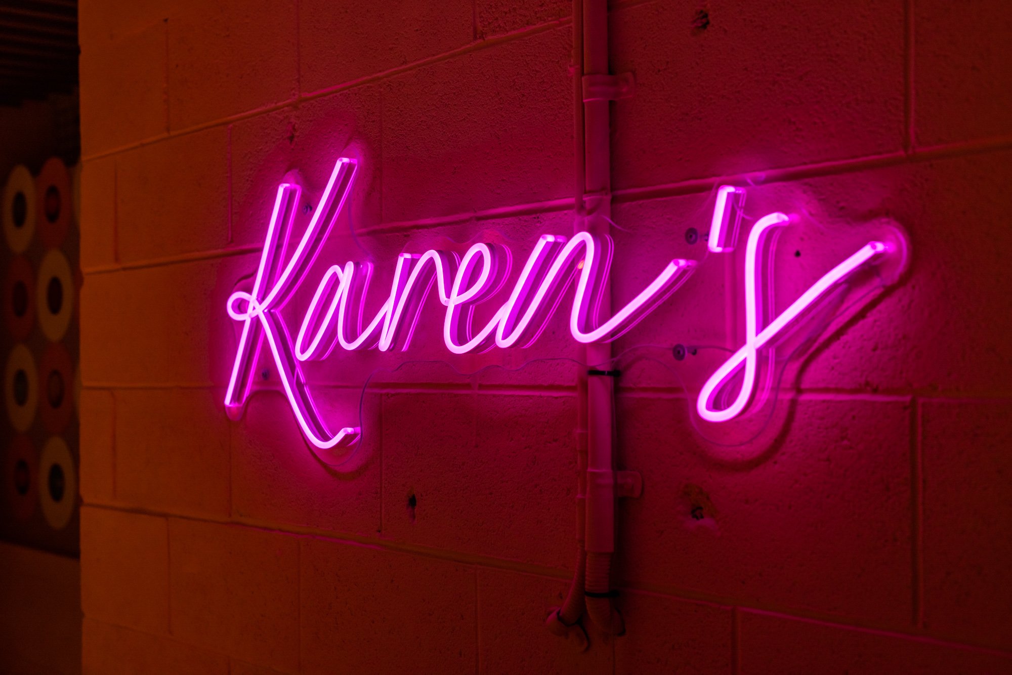 Pink neon sign on a brick wall spelling 'Karen' with an arrow.