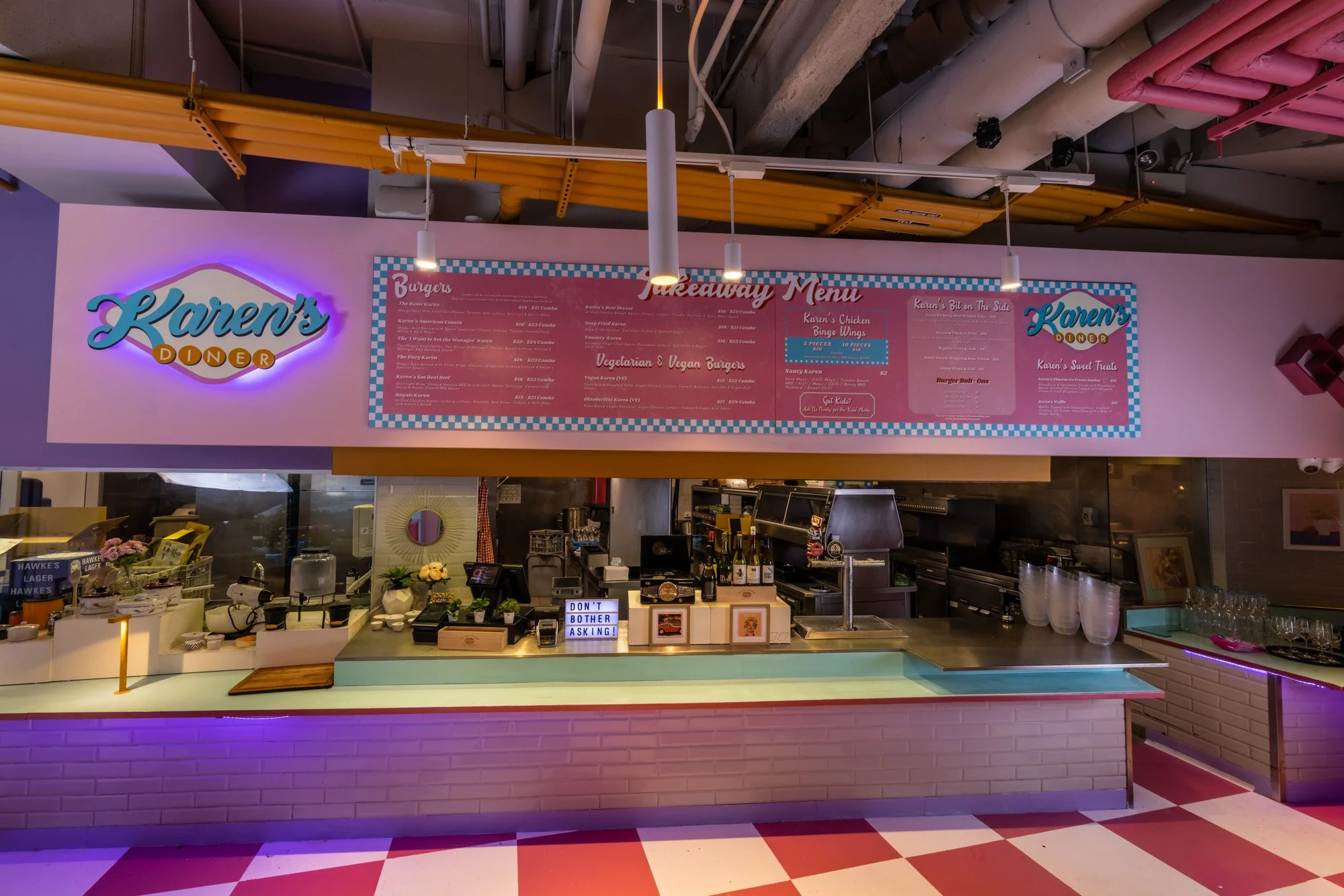 Counter at Karen's Doner restaurant with a pink neon sign, menu board overhead, and a small sign on the counter that says 'Don't bother asking!'.