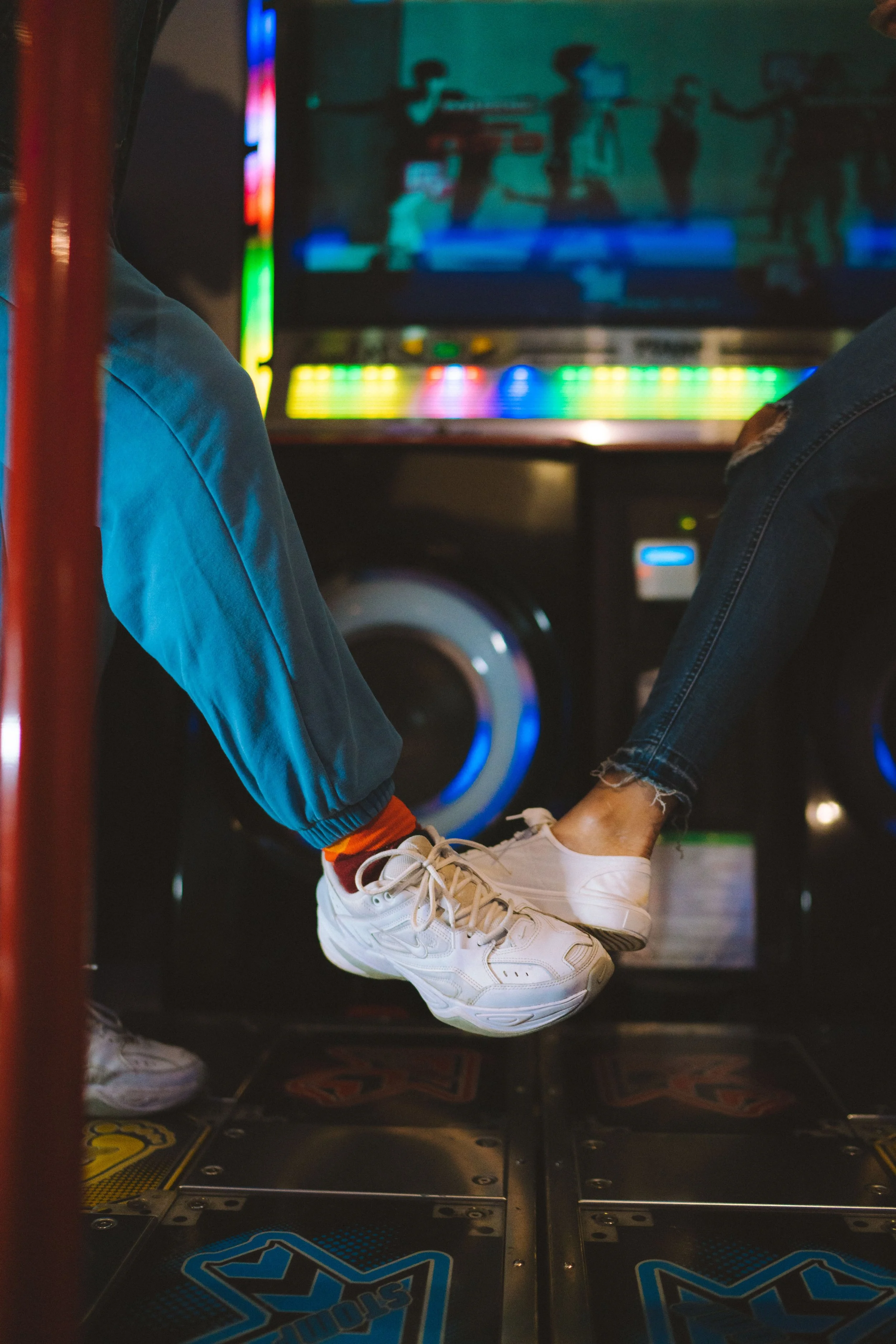 People sitting at an arcade, playing dance or rhythm video games with their feet on the dance pads.