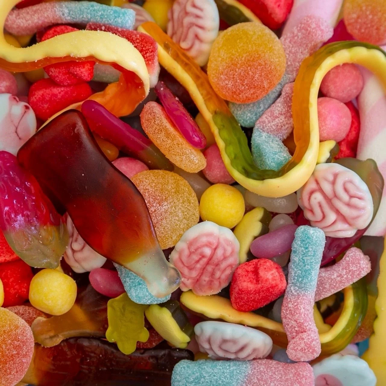 Assorted colorful candies including gummy worms, gummy brains, sugar-coated fruit slices, and jelly beans.