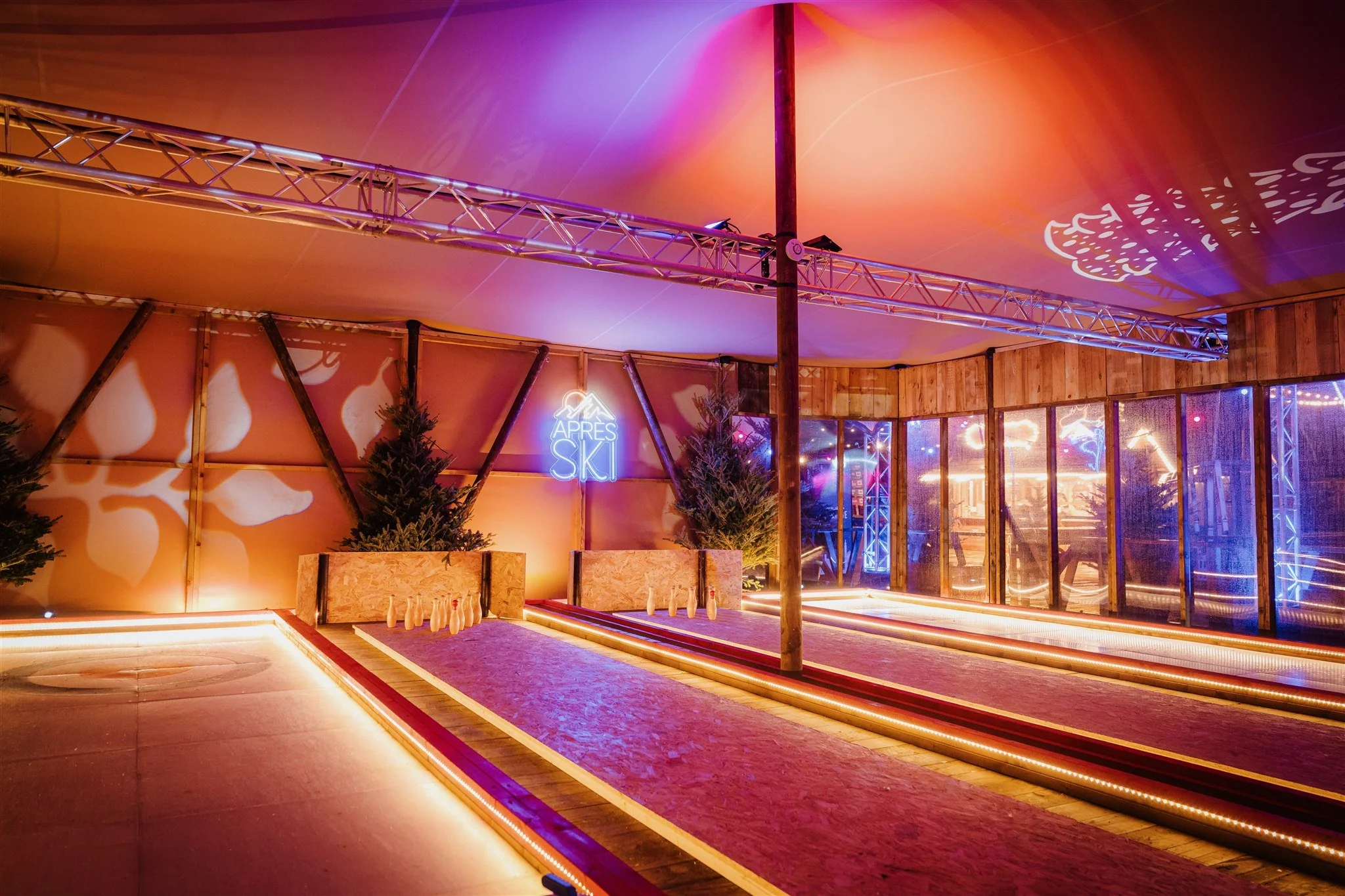 Indoor after ski bowling alley with neon sign reading 'Après Ski', Christmas trees, and illuminated pins.