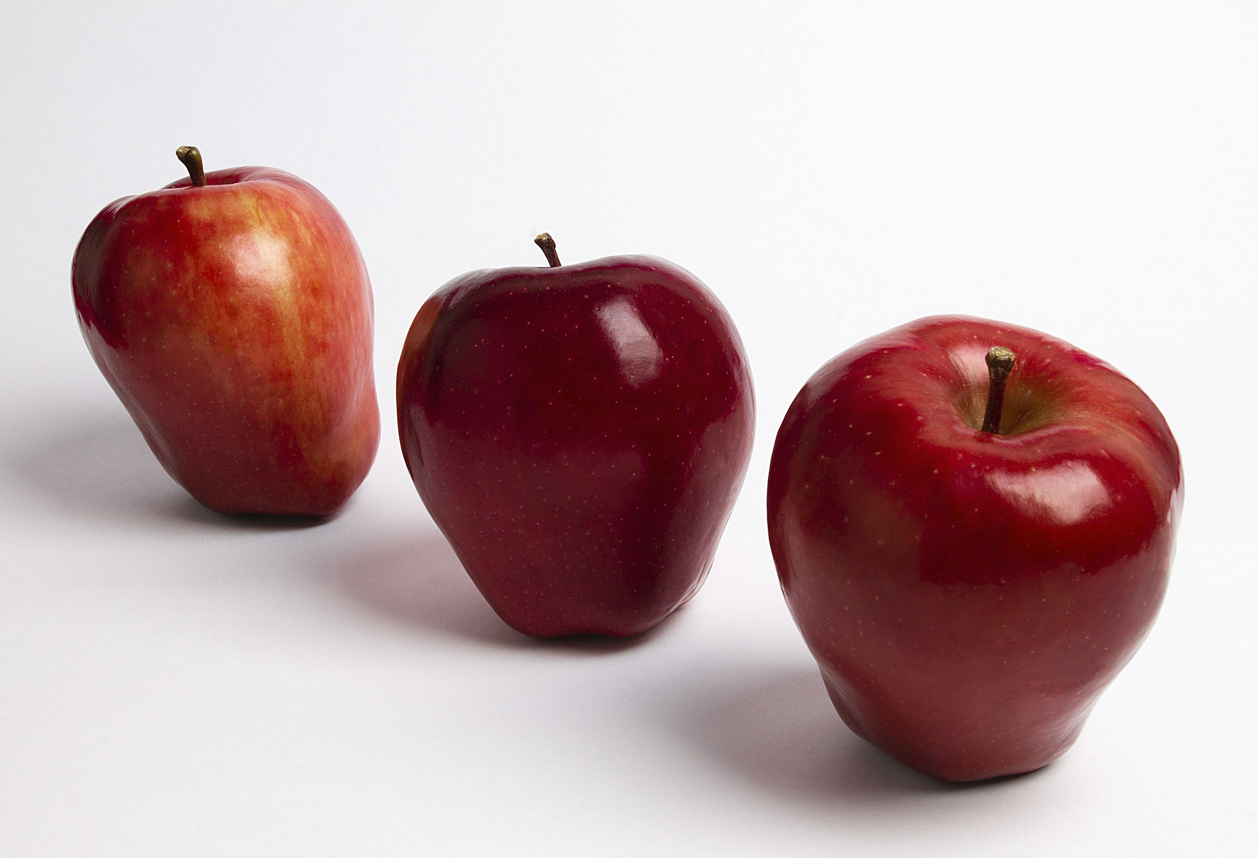 Three red apples on a white surface with a plain white background.