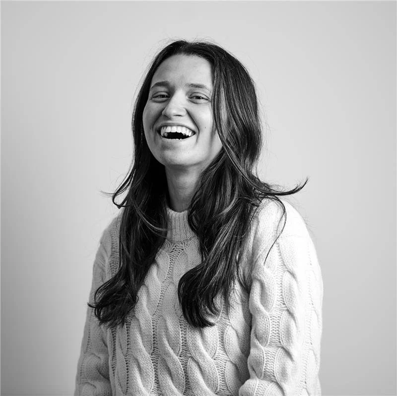 A black and white photo of a young woman with long hair, smiling and wearing a cable-knit sweater.