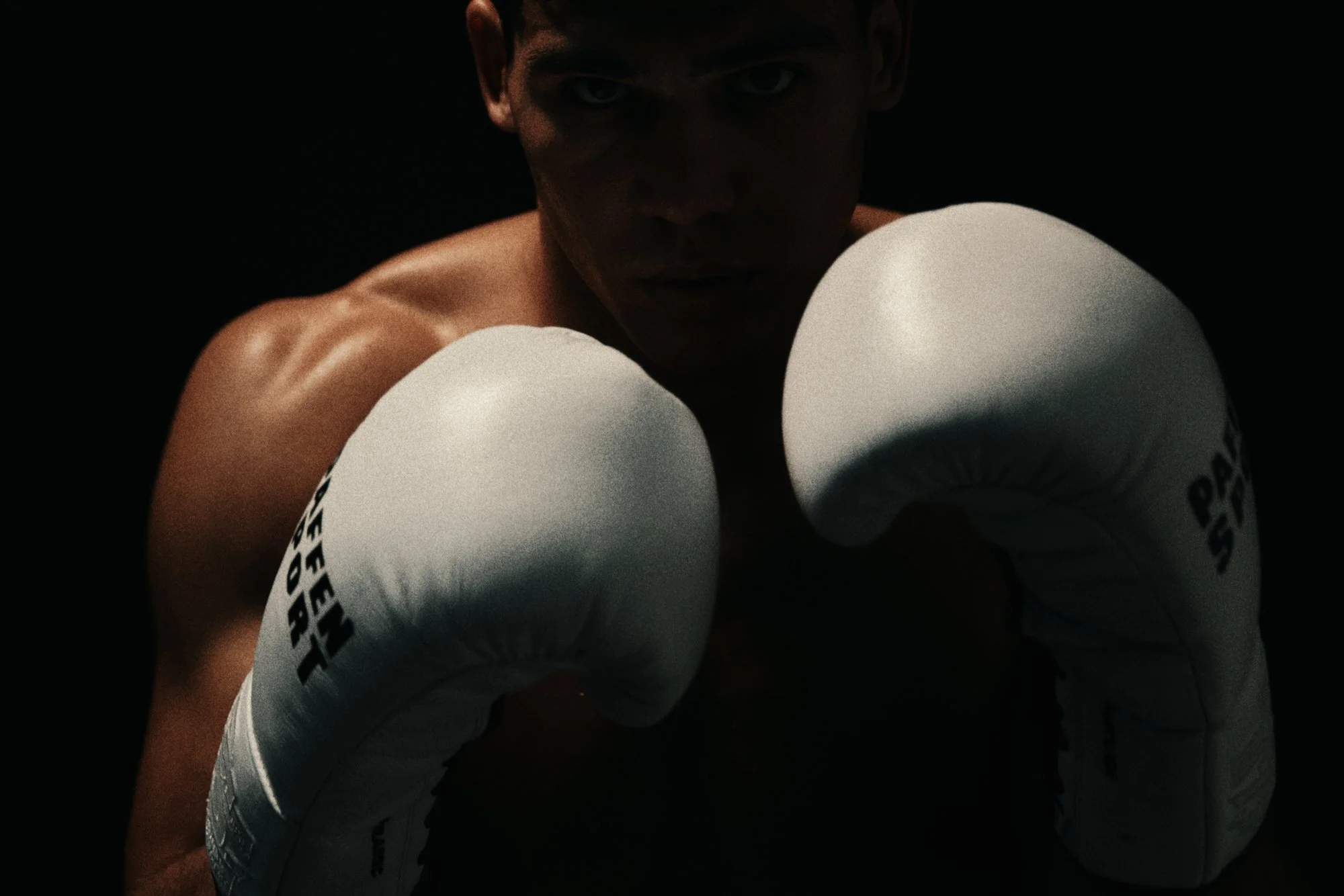 BOXER EMILIO ALVAREZ FACING THE CAMERA WITH HIS GLOVES RAISED, HIS FACE OUTLINED BY RIM LIGHT.