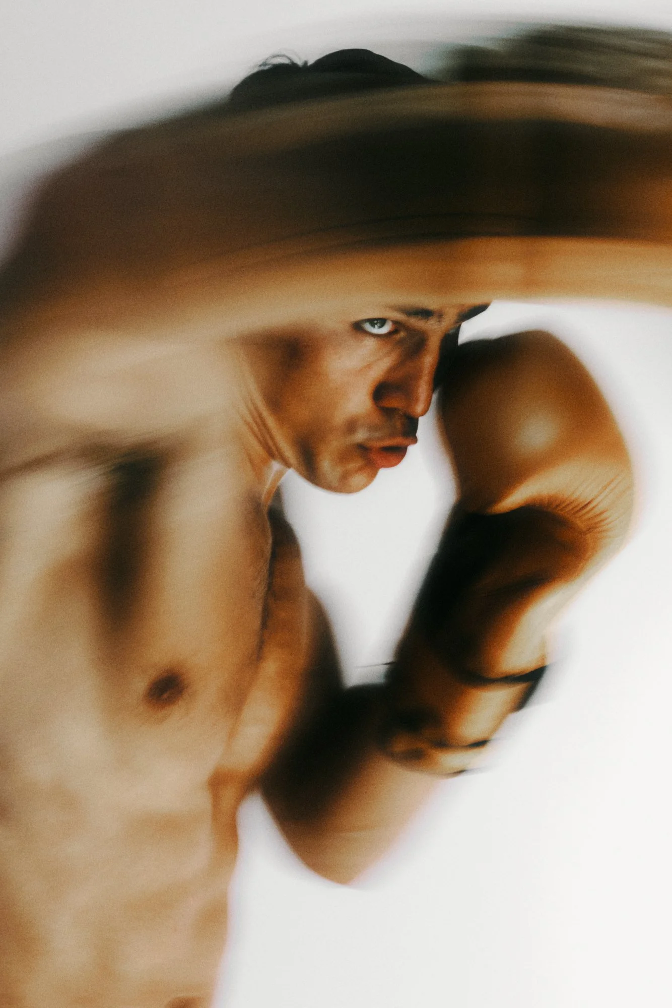BOXER EMILIO ALVAREZ WITH DARK HAIR AND LIGHT EYES, LOOKING INTENTLY, WITH HIS ARM BENT AND SUPPORTING HIS HEAD.