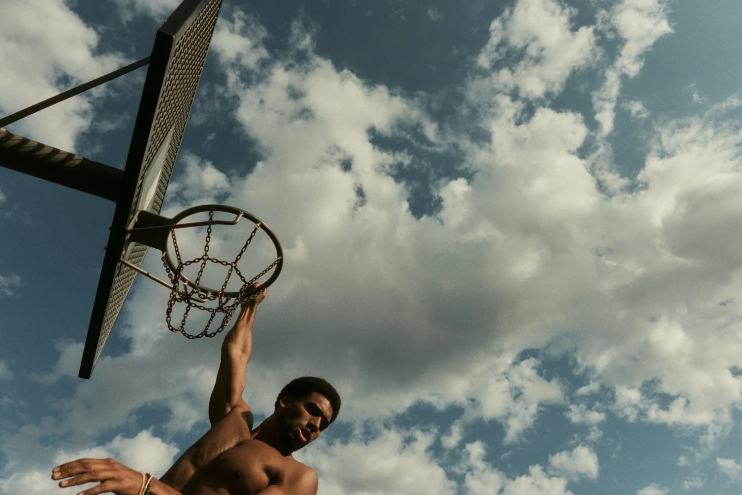 BASKETBALL PLAYER HANGING FROM AN OUTDOOR HOOP BENEATH A CLOUDY SKY IN BERLIN.