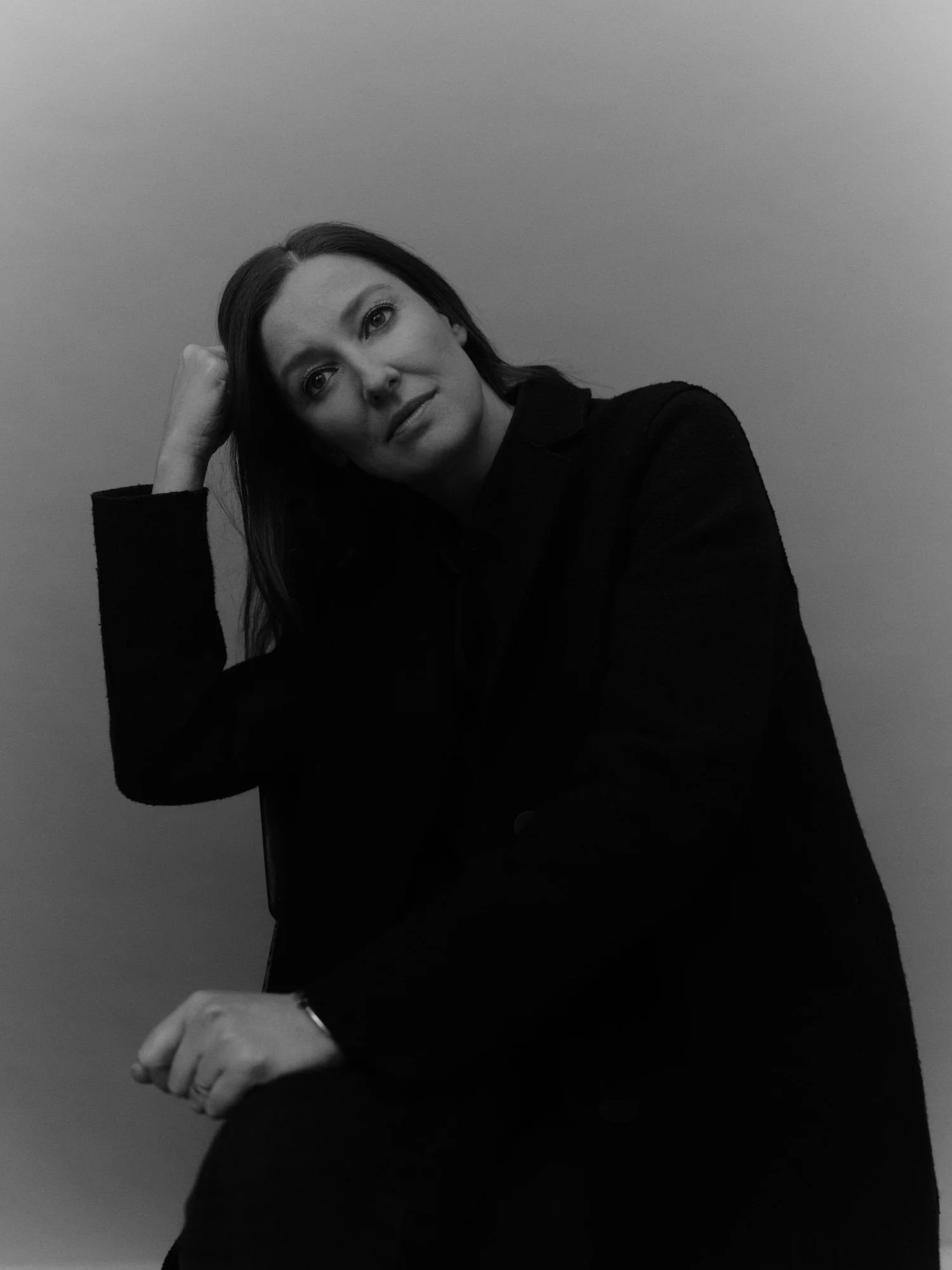 A BLACK AND WHITE PHOTO OF ACTOR ALEXANDRA MARIA LARA WITH DARK HAIR, RESTING HER HEAD ON HER HAND, DRESSED IN DARK CLOTHING, SITTING AGAINST A PLAIN BACKGROUND.