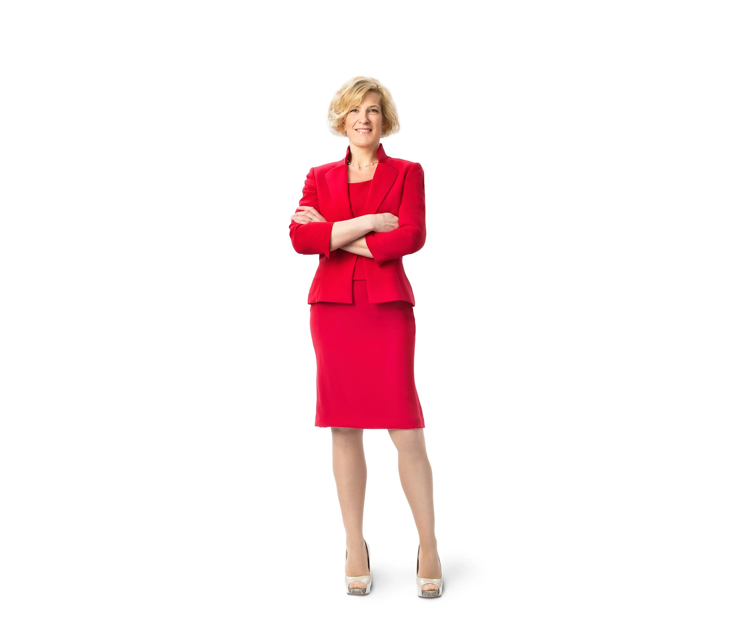 A full-length business portrait of a smiling woman wearing a bright red suit and standing with folded arms.