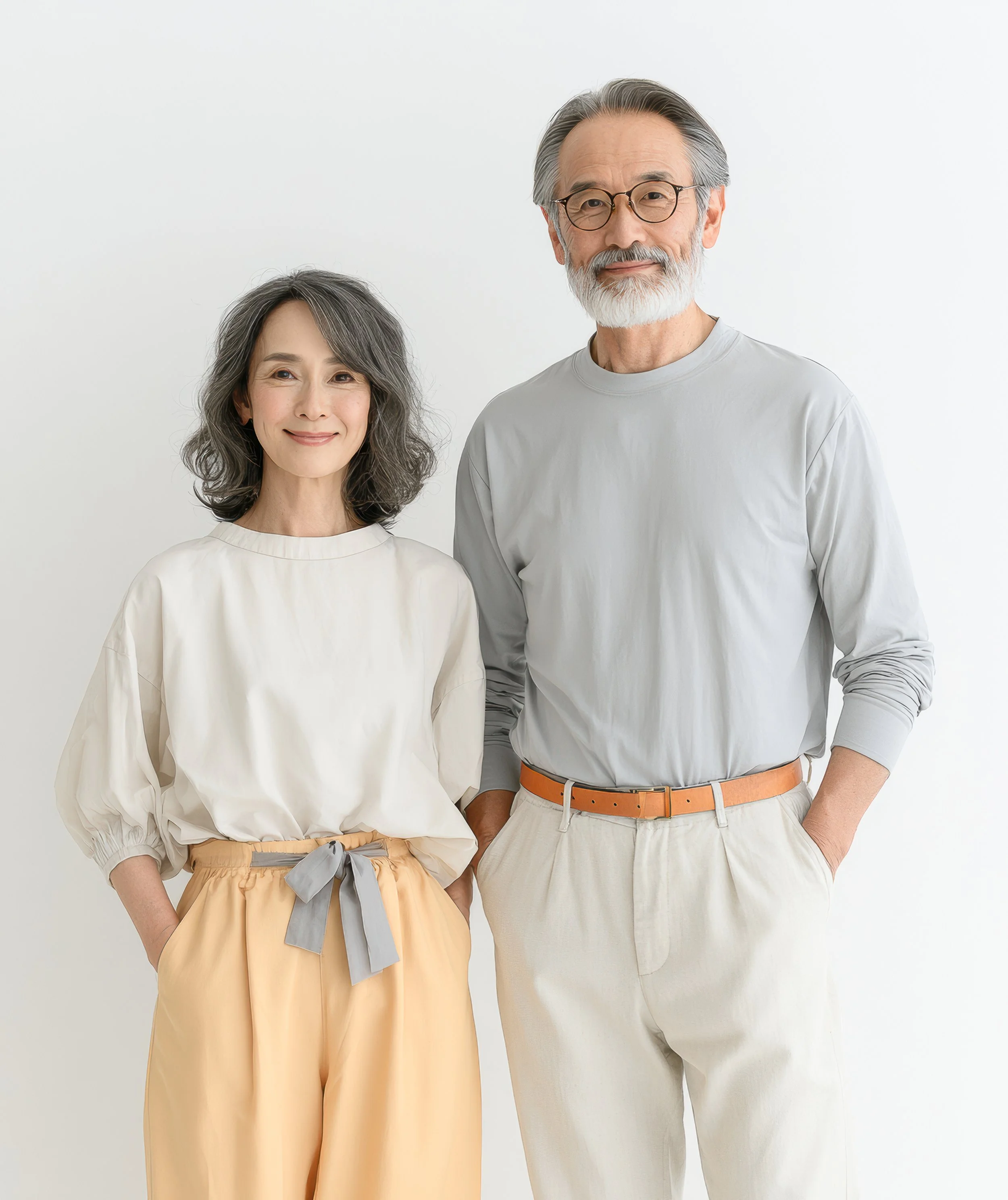 A relaxed portrait of a mature couple standing together in light-colored clothing against a white background.