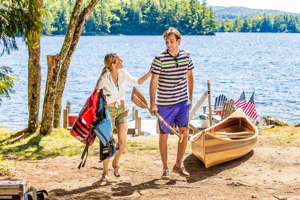 A young couple returning from a beautiful canoe ride along the shore of Lake Winnipesaukee, both smiling.