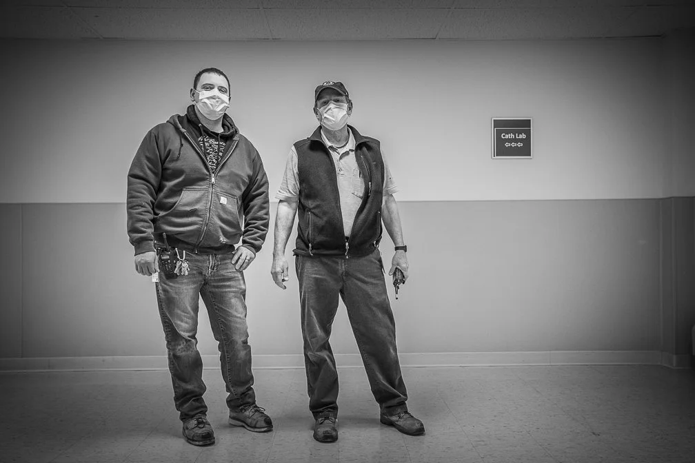 Two maintenance workers pause in a hospital hallway for a portrait, showcasing their role during the Covid pandemic.