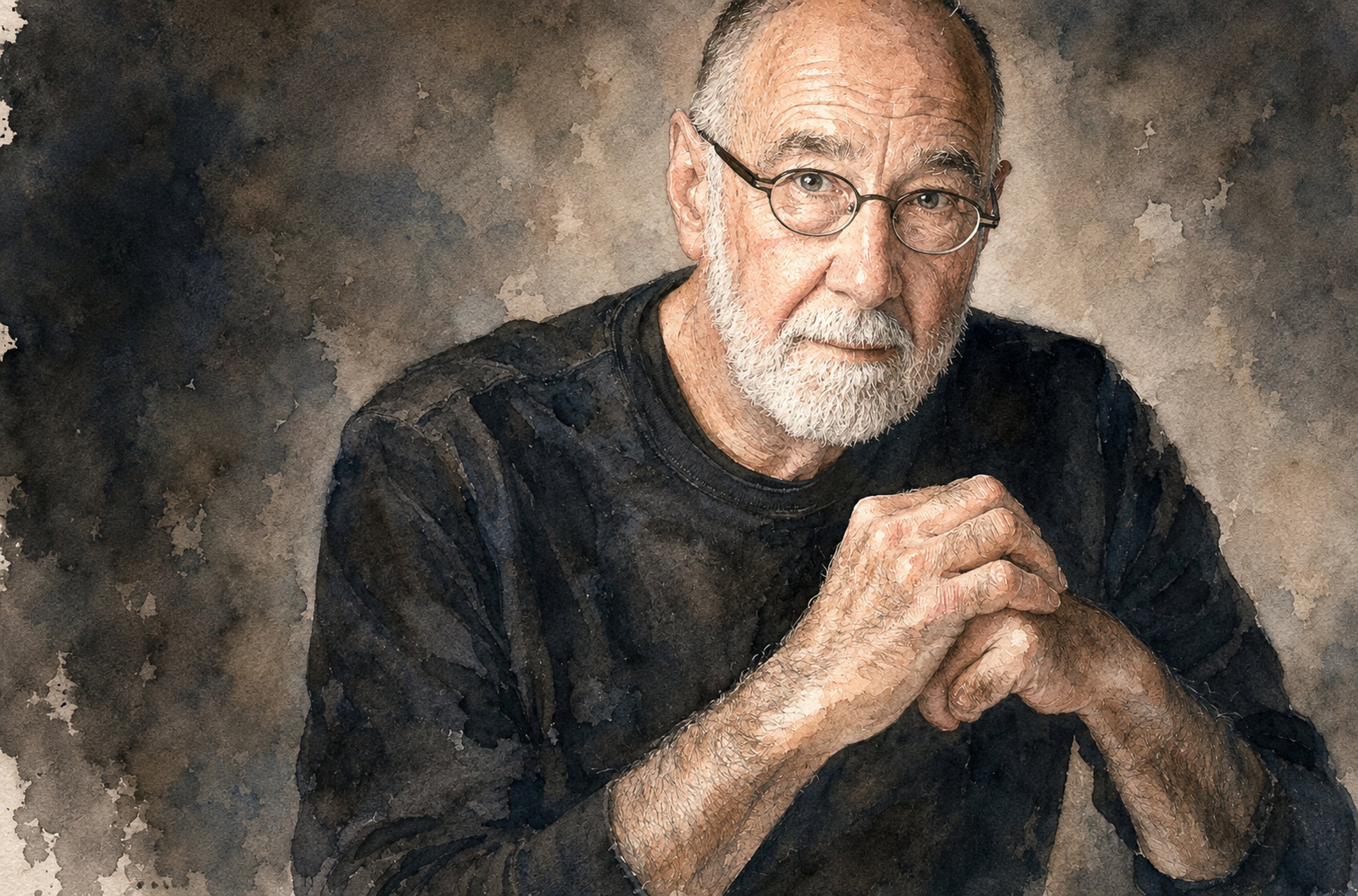 Close-up of an Artist Photographer with glasses, white beard, wearing a black shirt, with hands clasped together, against a textured dark background.