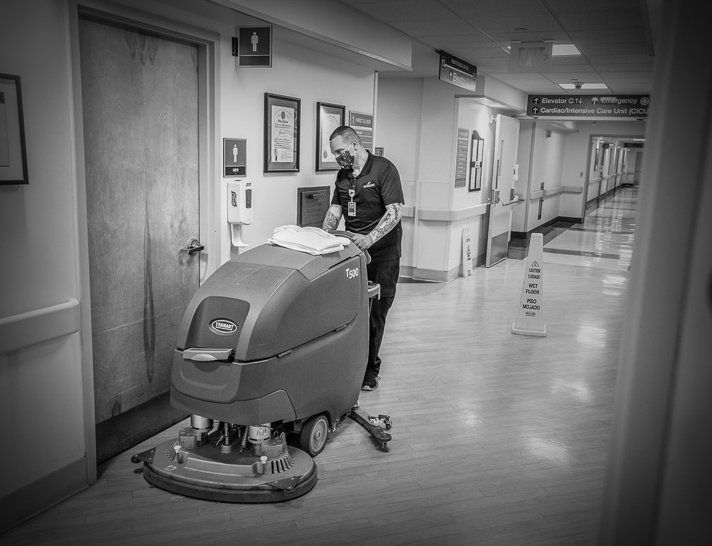 A cleaning services professional driving a large cleaning machine, washing and disinfecting the hospital floors.