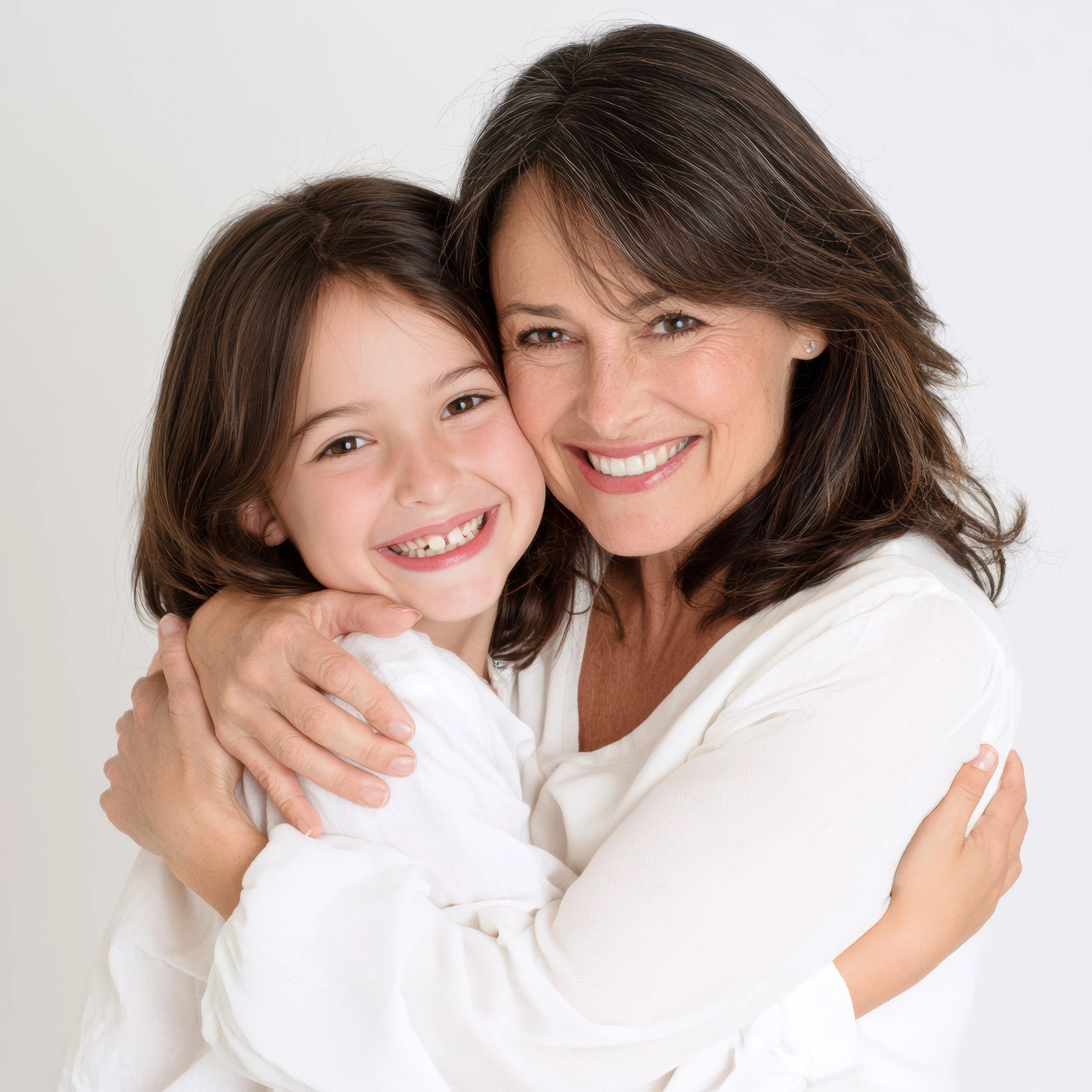 A warmly smiling woman and young girl embracing against a bright white studio background.