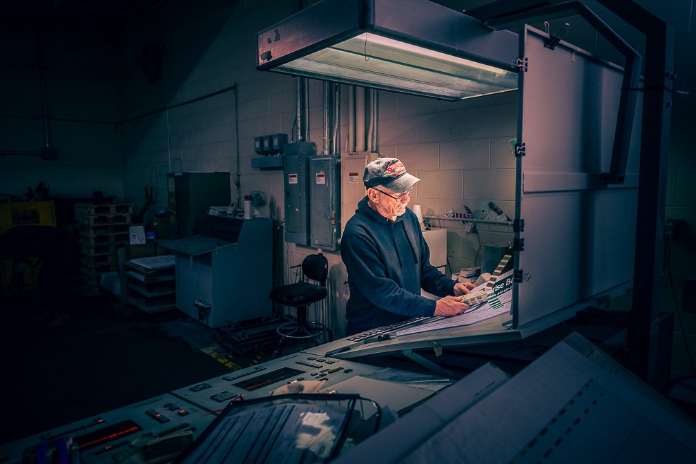 A print shop worker meticulously checking color samples at a light booth.