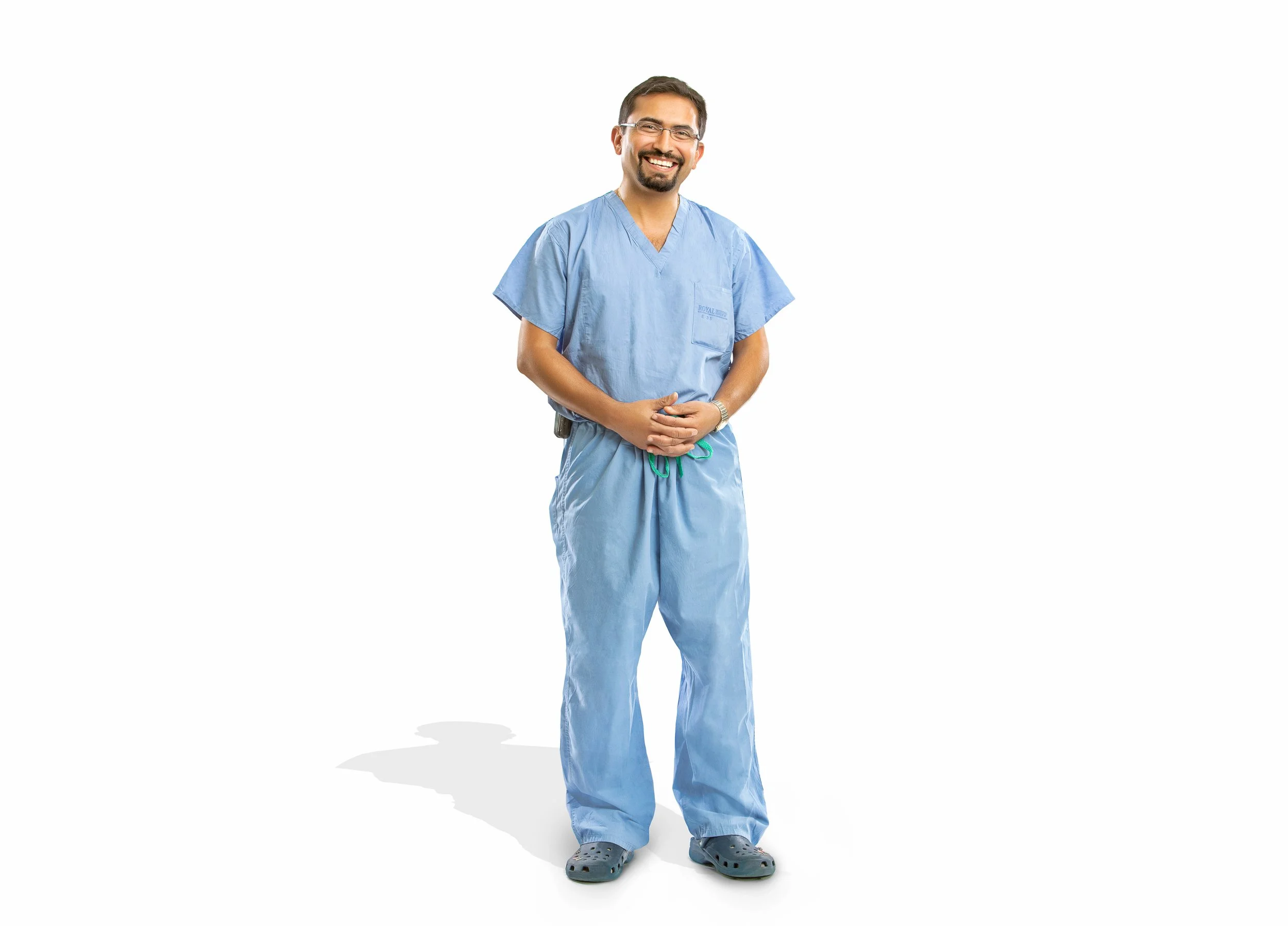A full-length portrait of a smiling healthcare professional wearing blue medical scrubs against a white background.