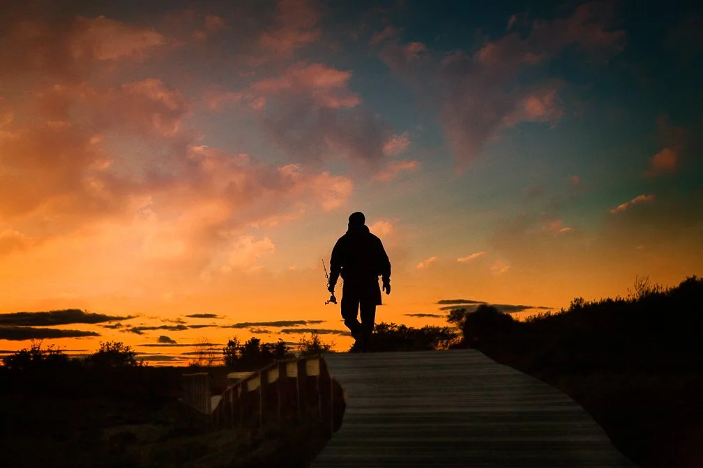 A fisherman walking along the boardwalk, silhouetted as he carries his fishing rod in Newburyport, MA.