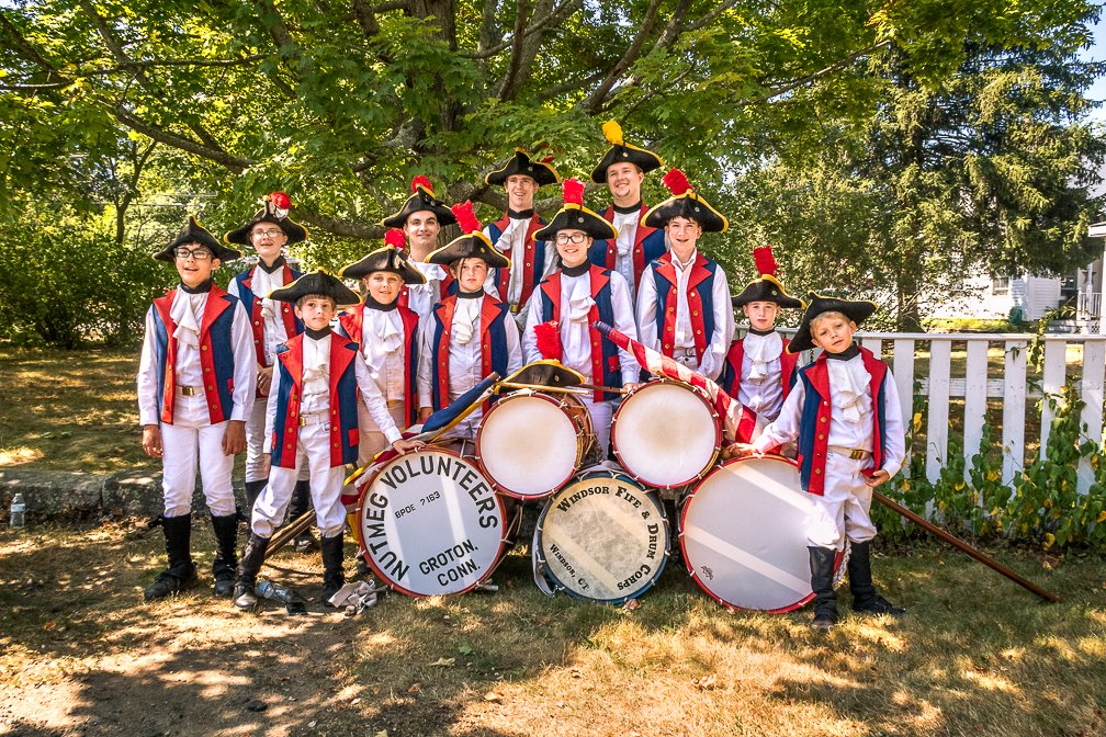 A drum and bugle team posing for a group photo, all smiling and wearing Minuteman costumes.