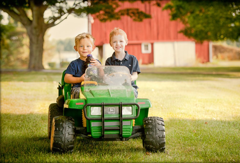 Two young boys sitting in a toy farm tractor, smiling and holding a bottle of Welch’s grape juice.