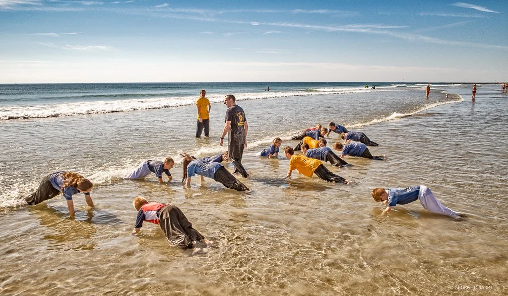 A karate class of young children practicing pushups outside at the NH oceanside shoreline,