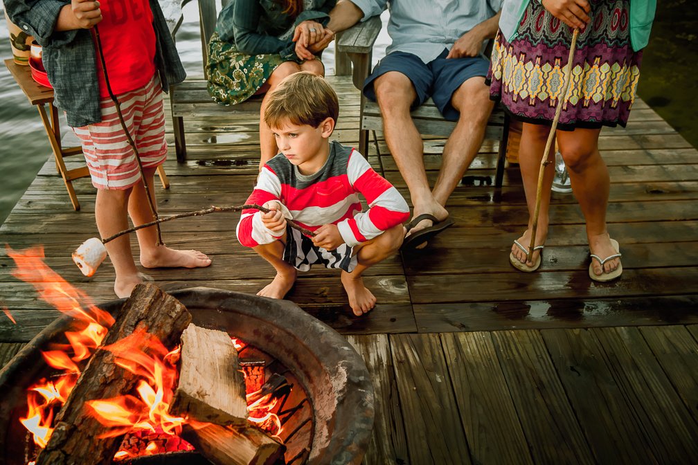 A family enjoying their summer lakefront vacation, with a young boy roasting marshmallows on a fire pit.