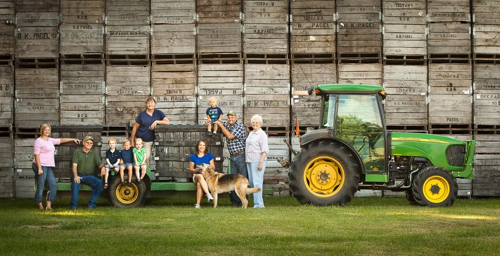 Three generations of a farm family posing with a huge farm tractor and their pet dog in PA.