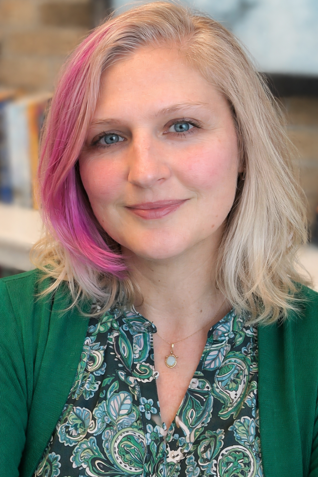 Image of author J.B. Vettori with blonde hair, blue eyes, wearing a green blouse and a turtle pendant necklace.